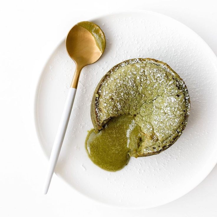 a white plate topped with a piece of cake covered in powdered sugar next to a spoon