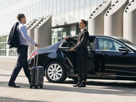 two men in suits and ties standing next to a black car with the door open