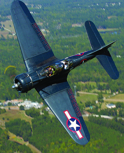 an airplane flying in the sky over a forest filled area with buildings and trees on both sides