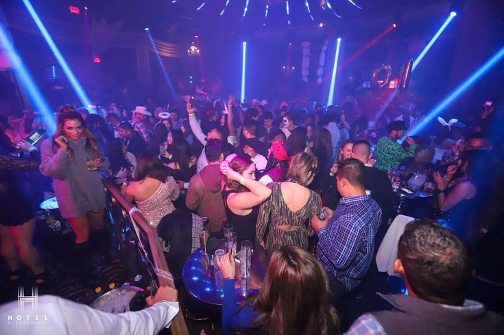 a group of people at a party with blue and purple lights on the ceiling, dancing