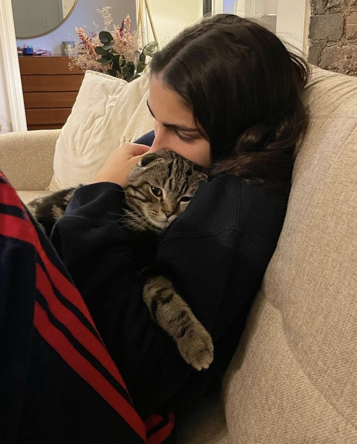 a woman laying on top of a couch holding a cat