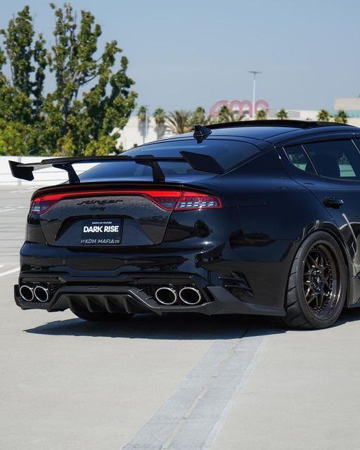 the rear end of a black sports car parked in a parking lot next to trees