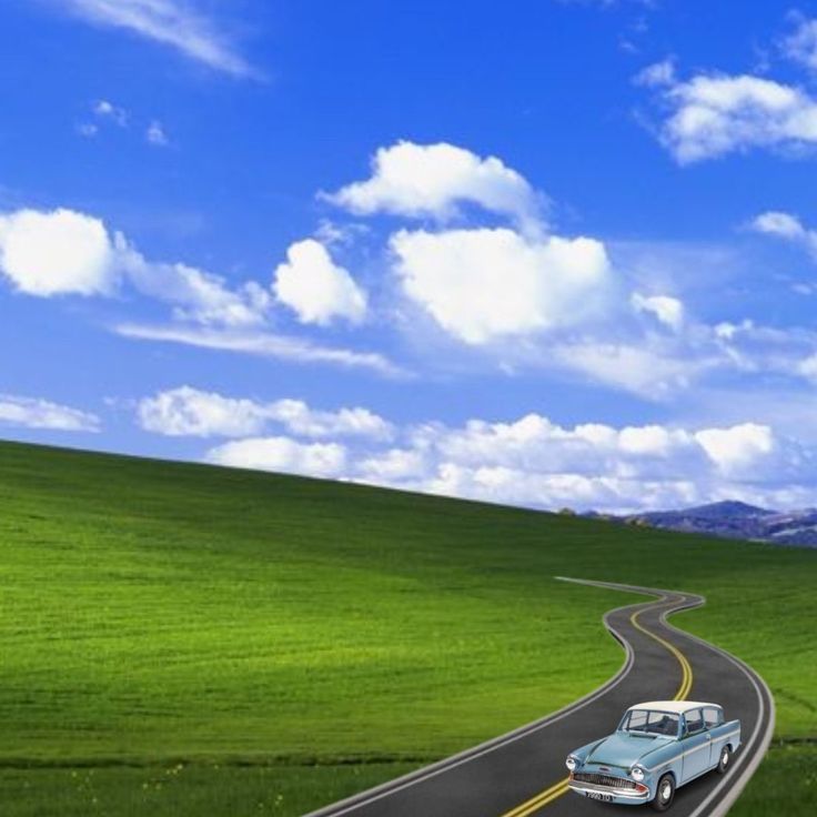 an old car driving down the road in front of a green field and blue sky