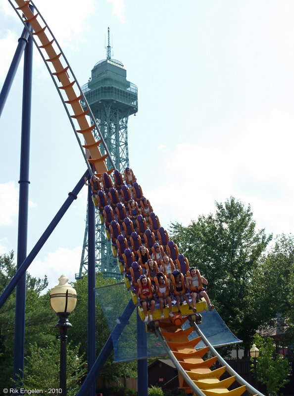 a roller coaster with people riding it in front of a tall tower and blue sky