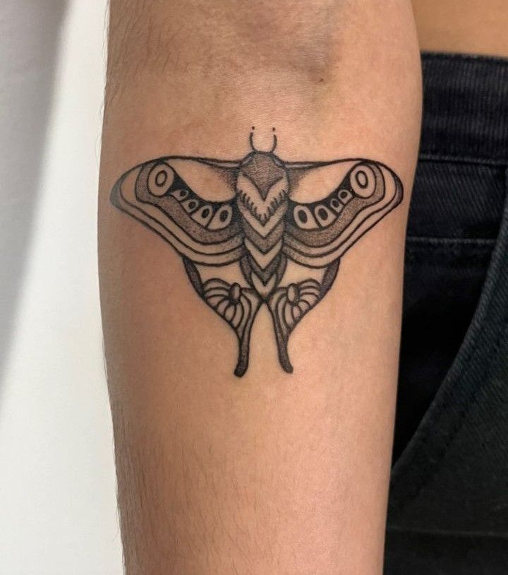 a small moth tattoo on the right arm and leg, with an intricate design in black ink