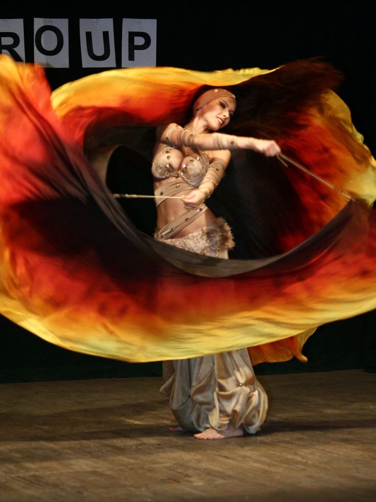 a woman is dancing with an orange and yellow flame around her body in the dark