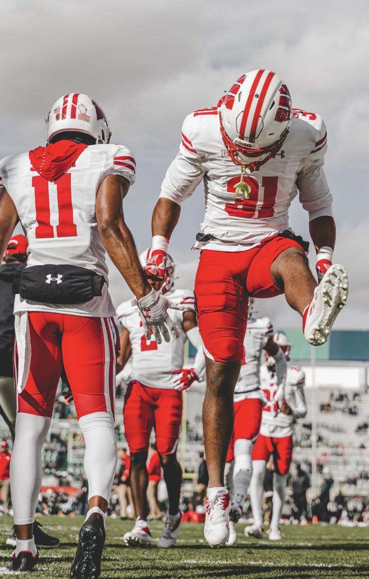 two football players in red and white uniforms are on the field with their feet up