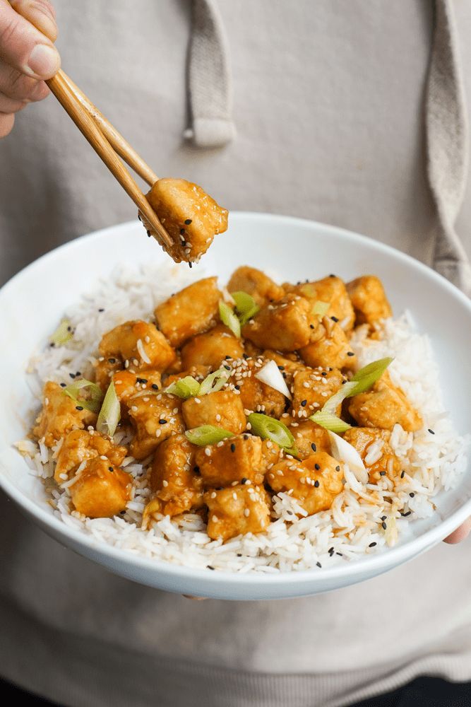 a person is holding chopsticks over a bowl of rice with chicken and vegetables