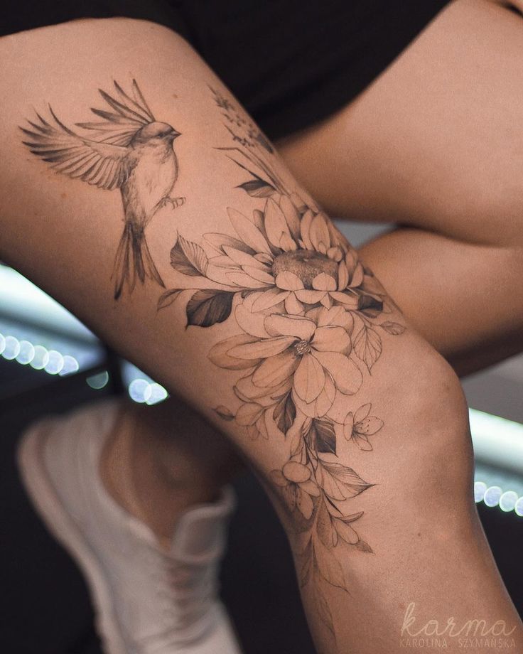 a woman's leg with flowers and birds on it, while she is sitting down