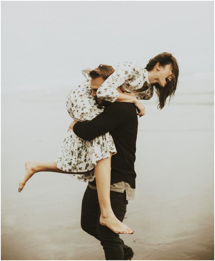 two people are hugging on the beach while one person is holding him up in the air