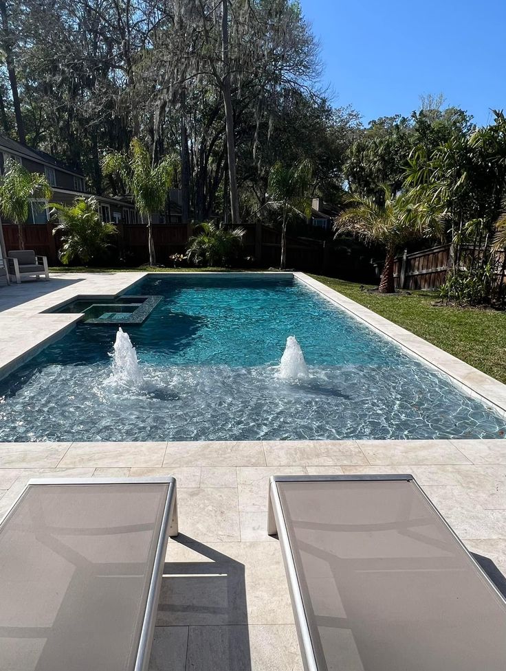 two lounge chairs sitting in front of a pool with water spouting from it