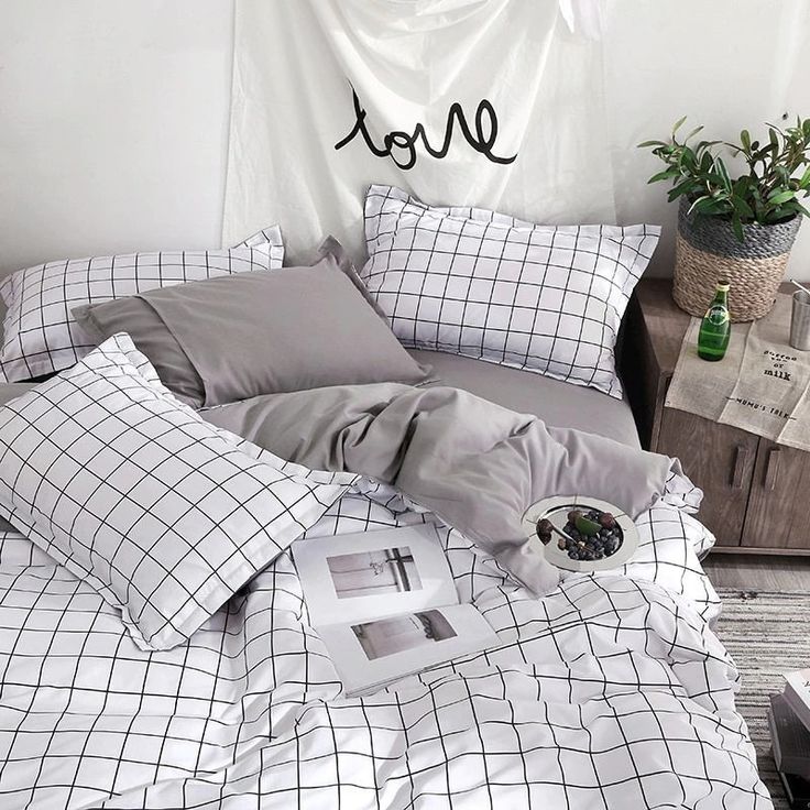 an unmade bed with grey and white sheets, pillows and pictures on the wall