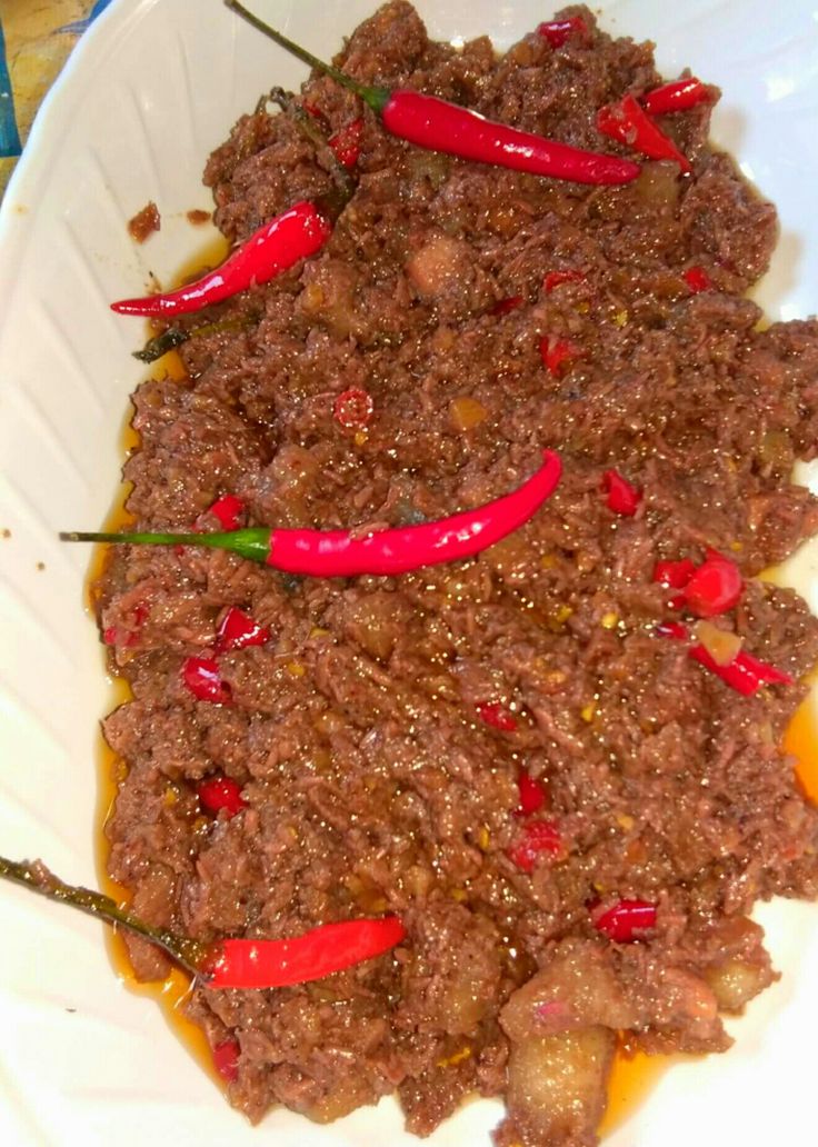 a white bowl filled with meat and peppers on top of a wooden table next to a bottle