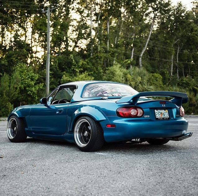 a blue sports car parked in a parking lot with trees in the backgroud