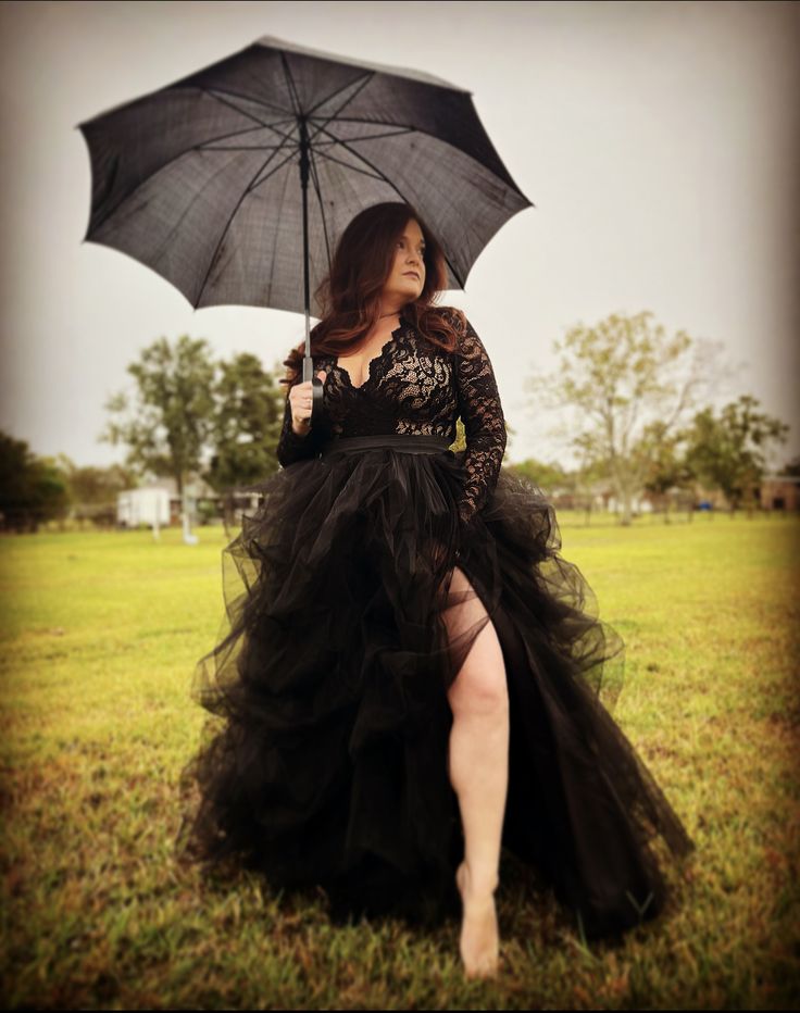 a woman in a black dress is holding an umbrella and posing for the camera with her legs crossed