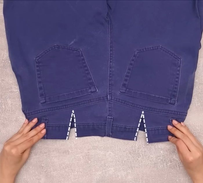 two hands are holding the back of a pair of blue jeans with white zippers