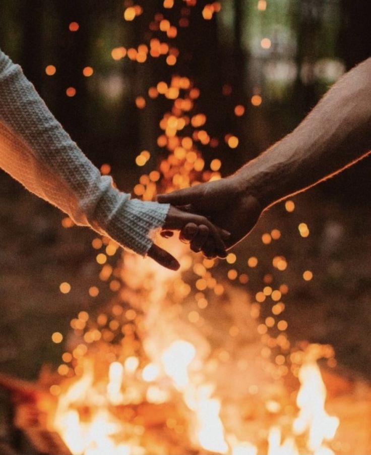 two people holding hands over an open fire