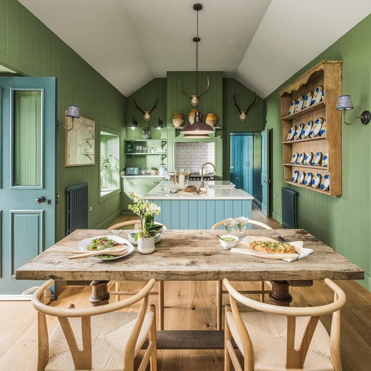 a kitchen with green walls and wooden table surrounded by chairs, plates on the counter