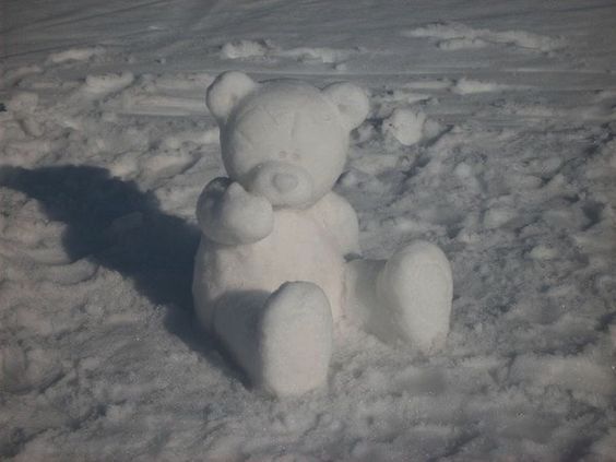 a large white teddy bear sitting in the snow with its shadow on it's back