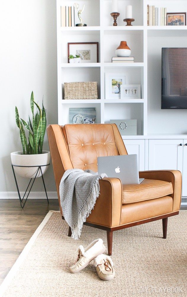 a laptop computer sitting on top of a brown chair in front of a white bookcase