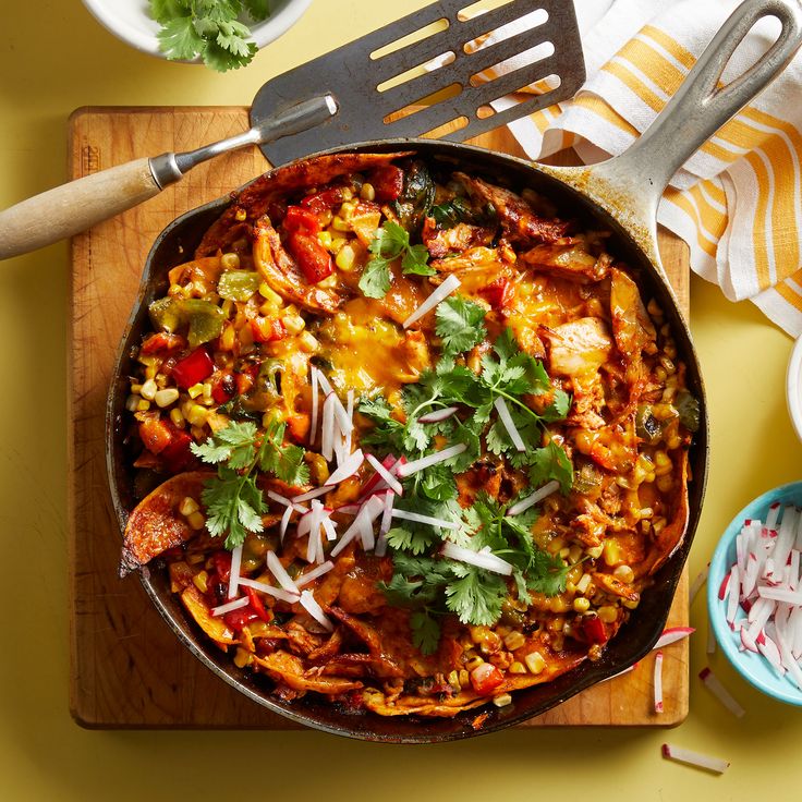 a skillet filled with mexican food and garnished with cilantro, limes, onions, corn