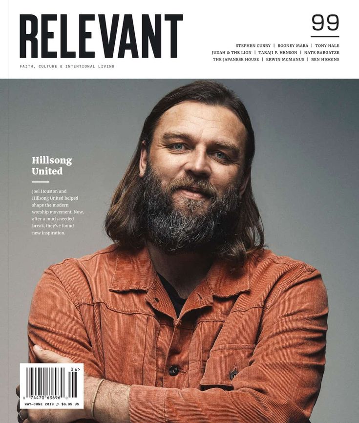 a man with long hair and beard standing in front of a magazine cover that reads relevant