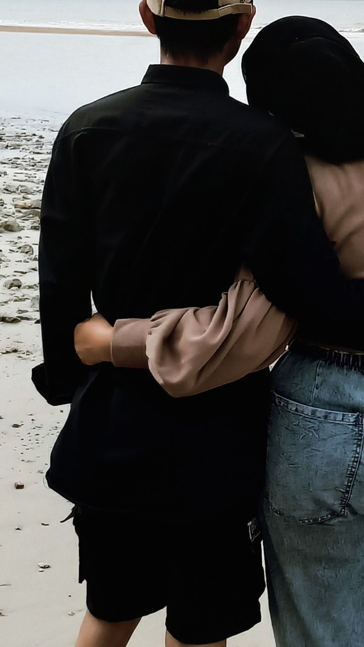 two people standing on the beach hugging each other