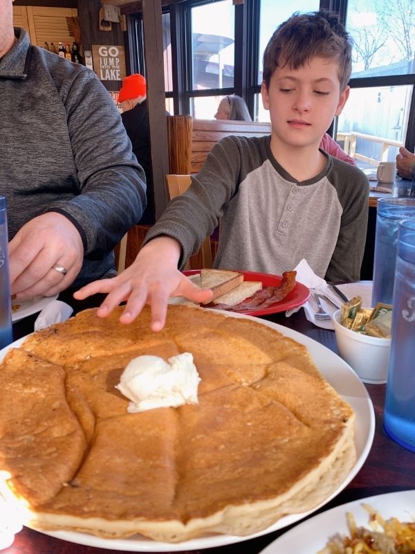 a man sitting at a table next to a child in front of a giant pancake