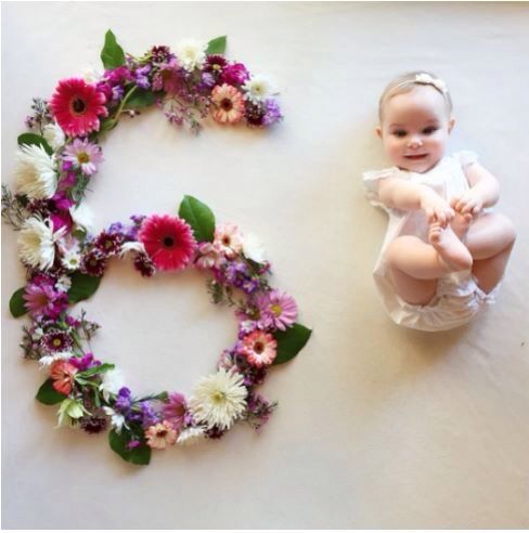 a baby sitting next to the number three made out of flowers and greenery on a white surface