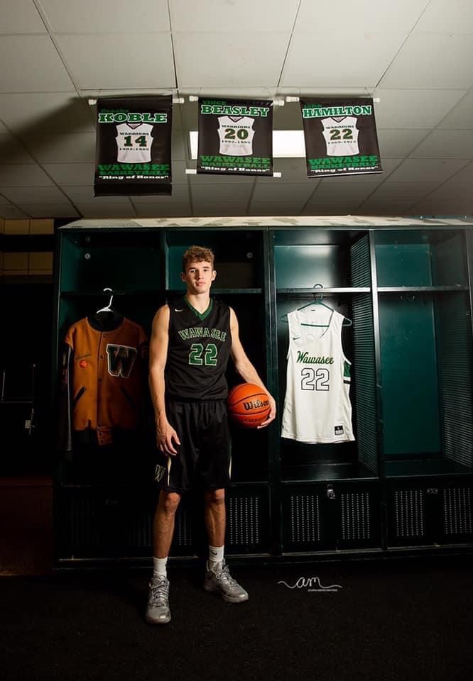 a young man holding a basketball standing in front of lockers with jerseys on them