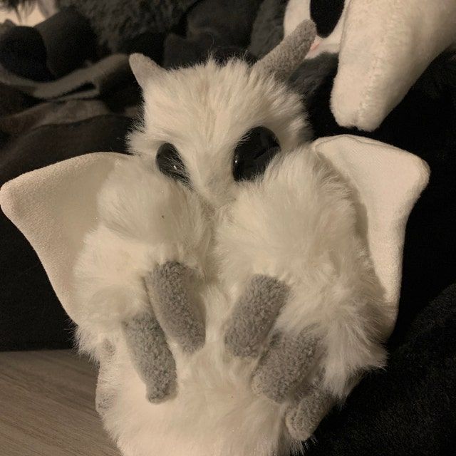 a white stuffed animal with black eyes and gray paws on it's back, sitting on a bed