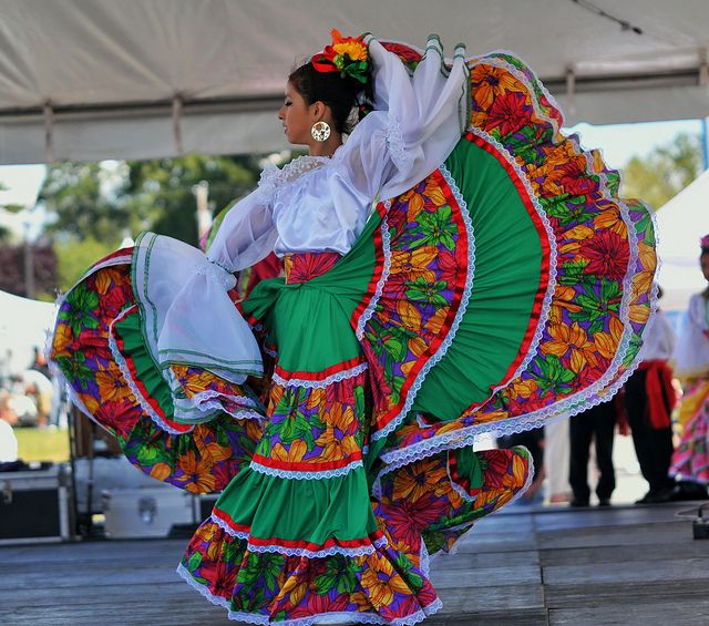 a woman in colorful dress dancing on stage with other people watching from the sidelines