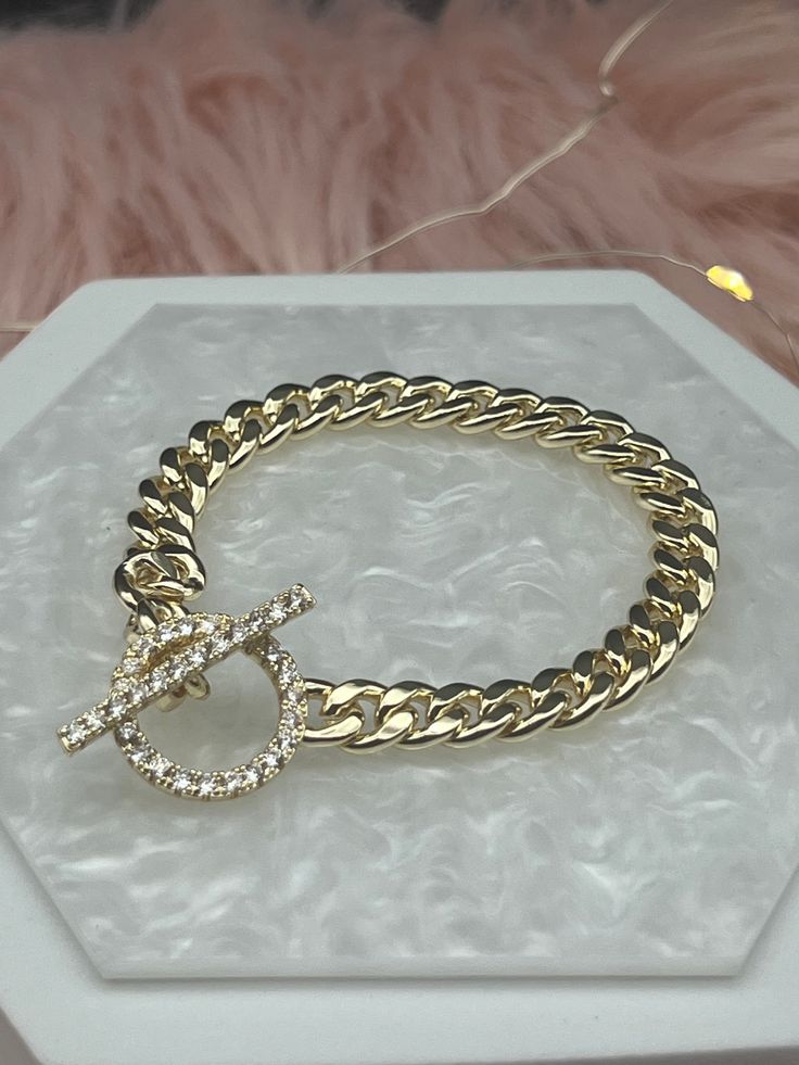 The Small Gold Chain Link CZ Toggle Bracelet is a delicate and sophisticated accessory, consisting of slender gold links with tiny cubic zirconia stones toggle clasp that add a subtle sparkle. Its toggle clasp provides a secure and stylish closure, making this bracelet an ideal choice for adding a touch of elegance to everyday outfits. Size: 6 3/4 inches - Inner Diameter Closure: Toggle Clasp Material: Brass with 18K Gold Plating with Rhodium Coating Lead Free and Hypoallergenic Sabika Inspired Jewelry, Small Gold Chain, Edgy Aesthetic, Valentines Sale, Black Leather Bracelet, Toggle Bracelet, Magnetic Bracelet, Design Jewelry, Toggle Clasp