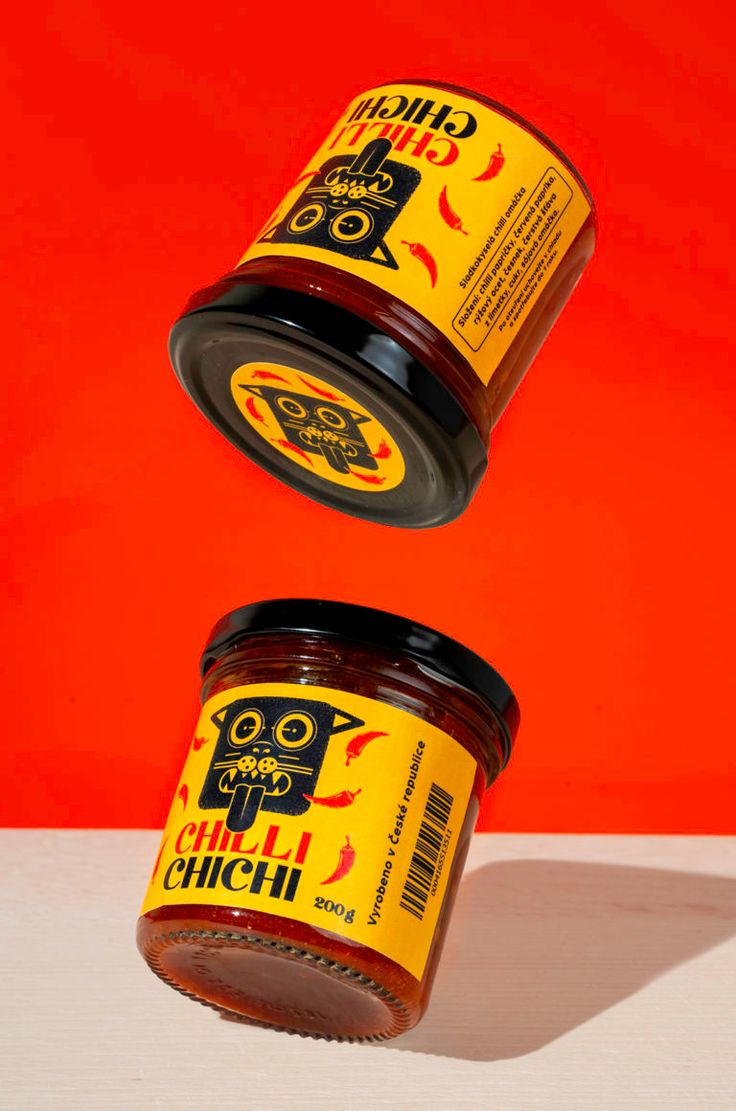 two jars of chili sauce sitting on top of a table next to an orange wall