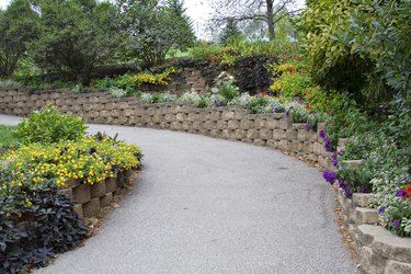 a garden with many different plants and flowers on the side of the road in front of a stone wall