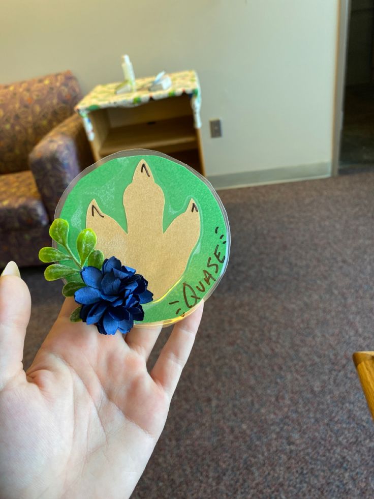 a person holding up a green and yellow brooch with blue flowers on it's finger