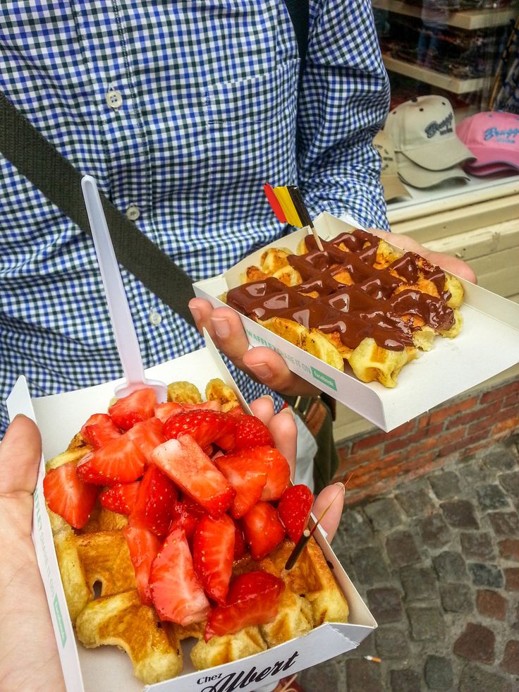 a person holding two boxes of waffles with strawberries on top and chocolate sauce