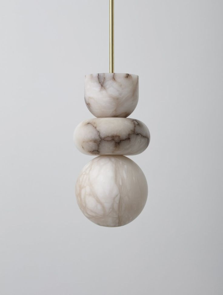 three white marble balls hanging from a gold colored hook on a gray background with reflection in the water