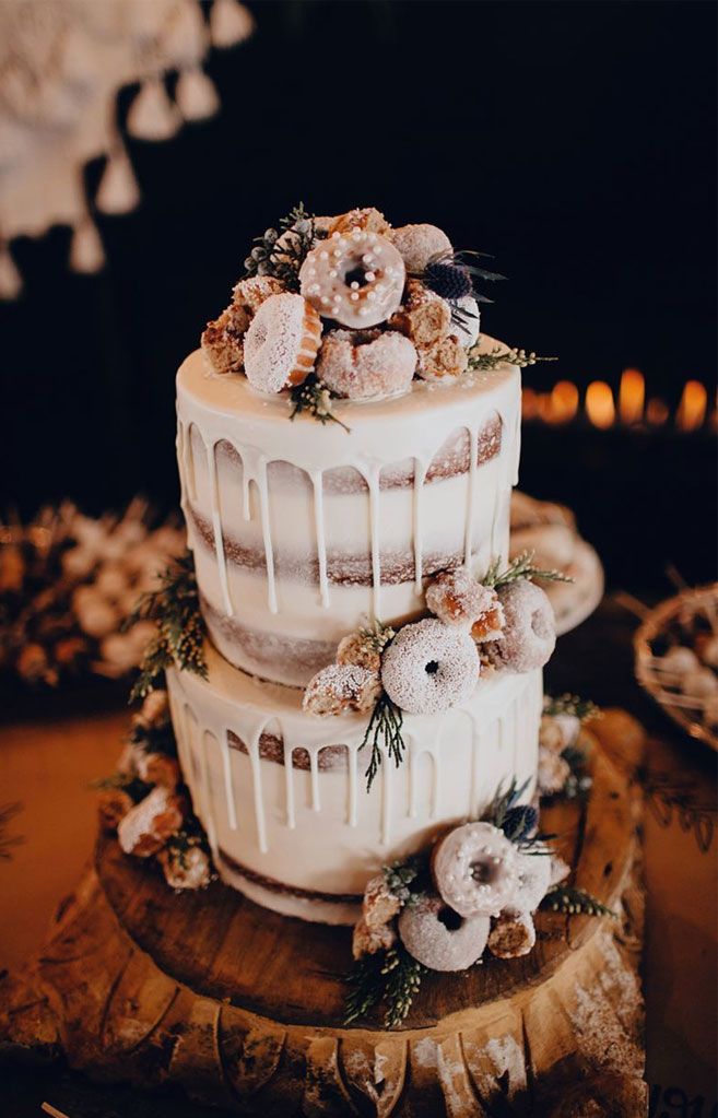 a three tiered cake with frosting and flowers sitting on top of a wooden slice