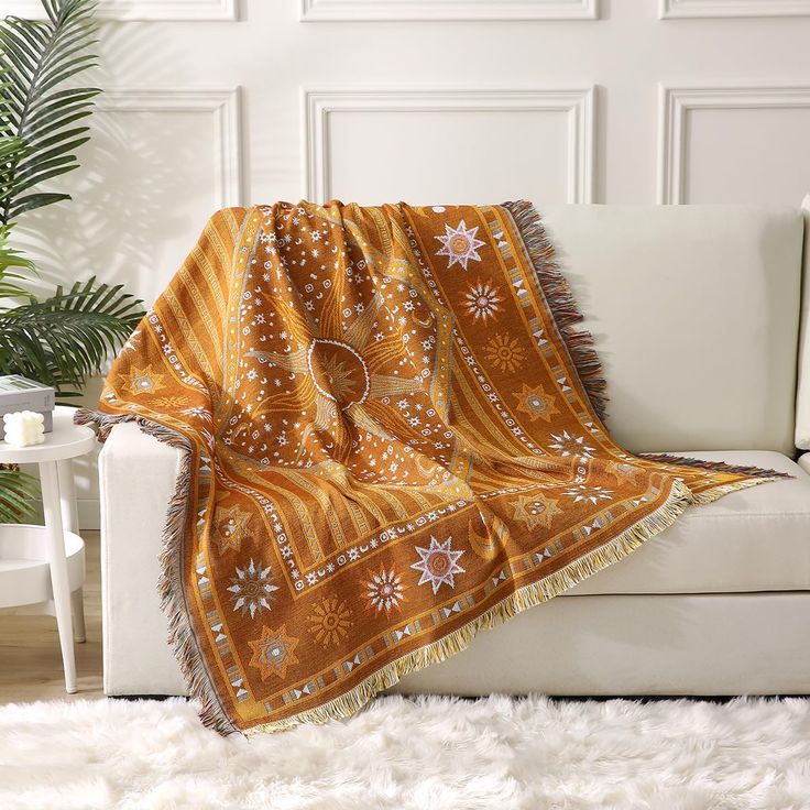 an orange and white blanket sitting on top of a couch next to a potted plant