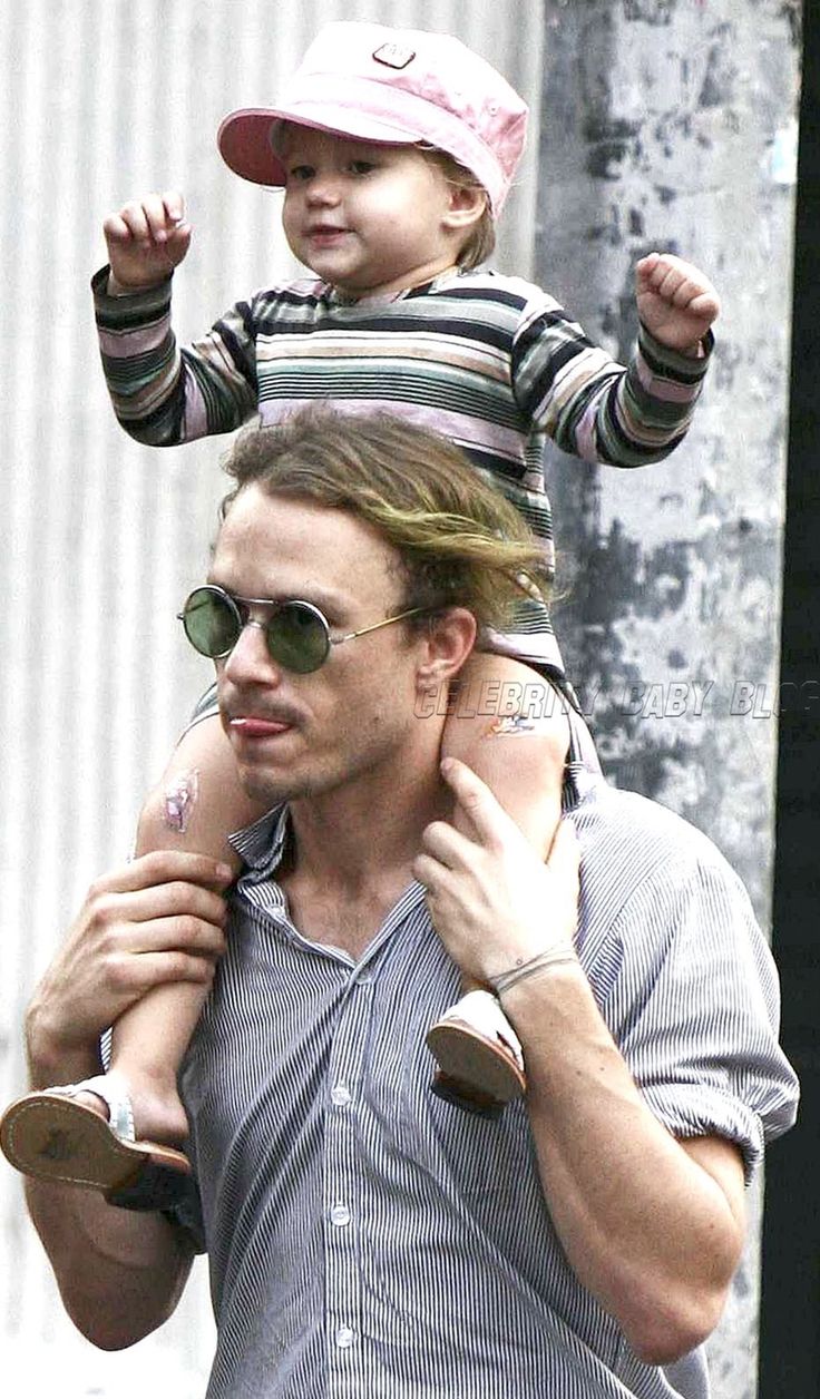 a man holding a small child on his shoulders while wearing sunglasses and a baseball cap