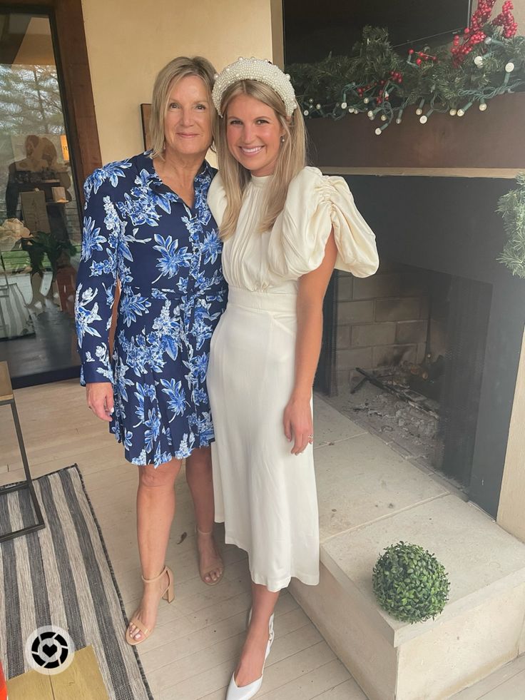 two women standing next to each other in front of a fire place with a plant