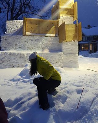 a woman kneeling down in the snow next to a building with stairs on top of it