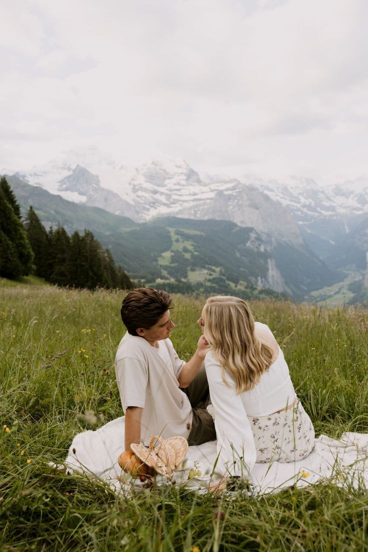 two women sitting in the grass with mountains in the background