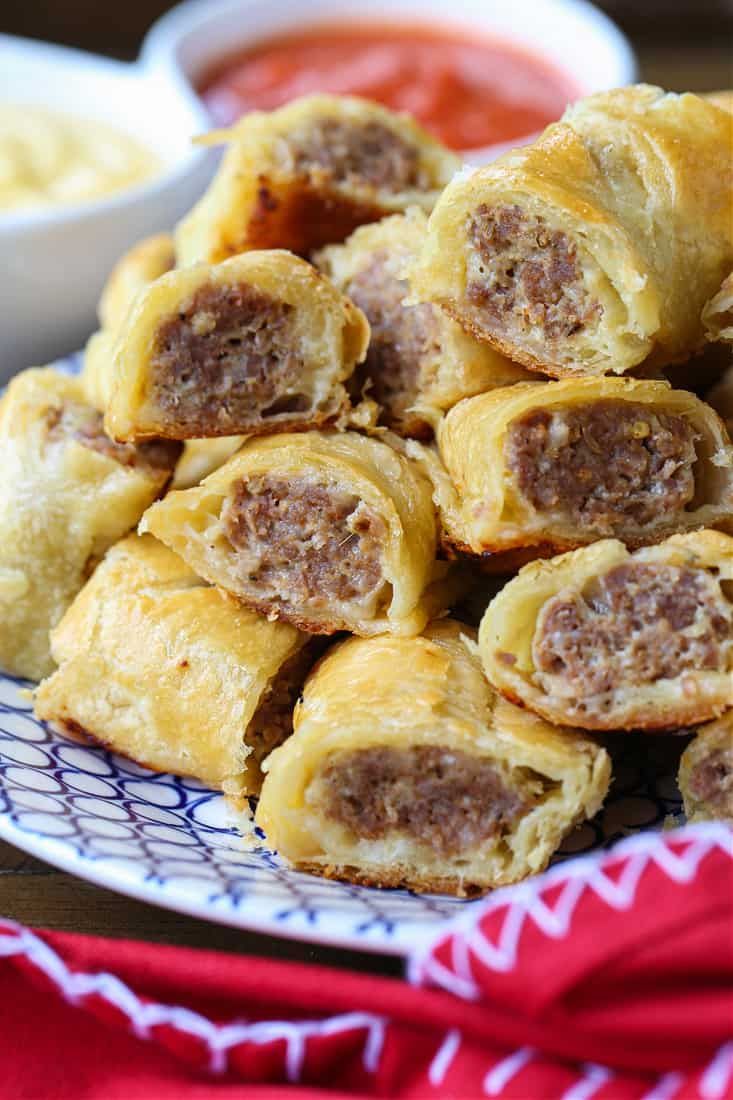 sausage rolls on a plate with dipping sauces in the backgroud and red cloth