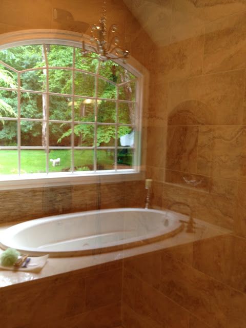 a bath tub sitting under a window next to a sink in a room with marble walls