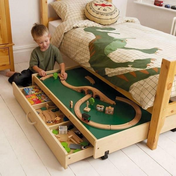 a young boy playing with his toy train set on the floor in front of a bed