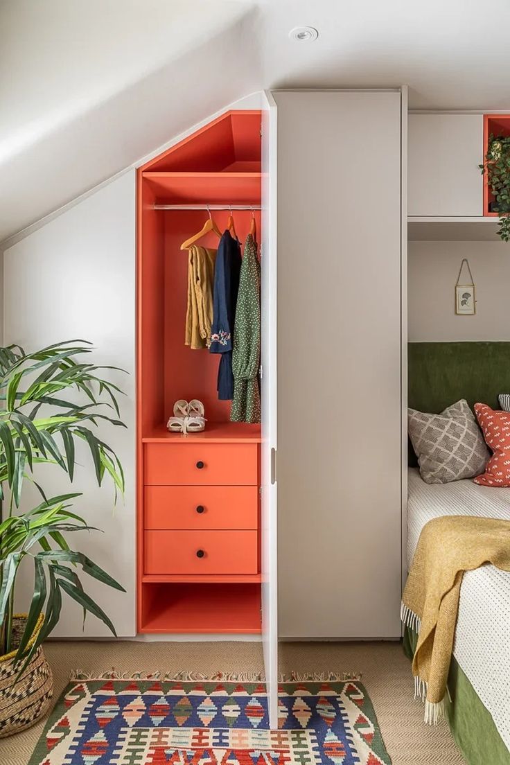 a bedroom with an orange bookcase next to a bed and a green plant in the corner