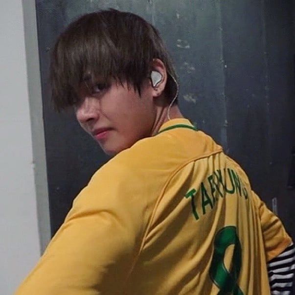 a boy with ear buds on his ears is standing in front of a mirror wearing a yellow shirt