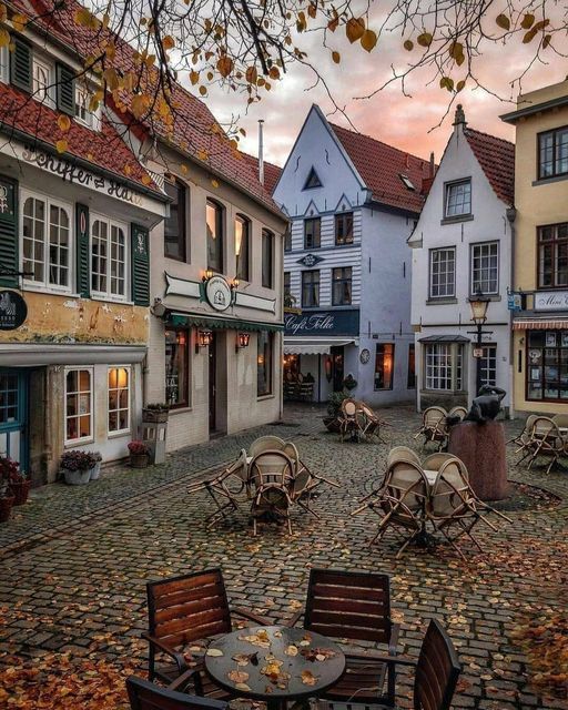 an old town with tables and chairs on the cobblestone street in autumn time